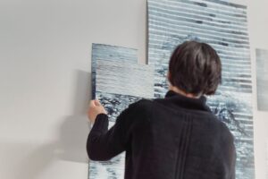 Person placerar ett blågrått konstverk bland målningar i ett galleri