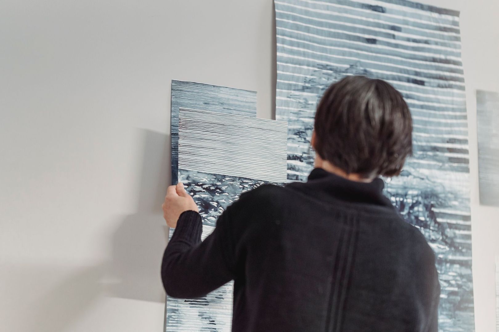 Person placerar ett blågrått konstverk bland målningar i ett galleri